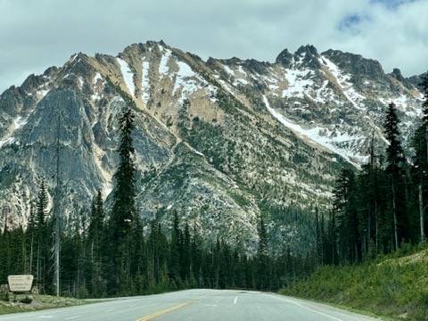 Scenic highway leading toward rugged, snow-dusted mountains surrounded by evergreen trees in North Cascades National Park.