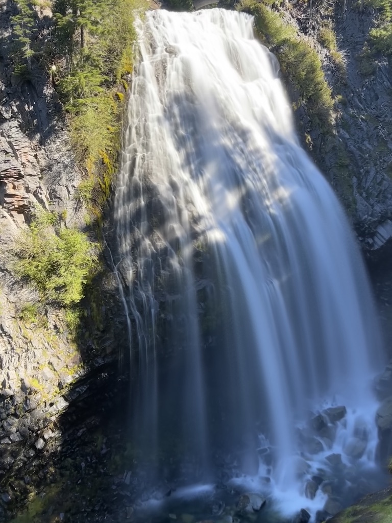 The powerful, cascading Narada Falls in Mount Rainier National Park, framed by rugged rocks and vibrant green foliage.