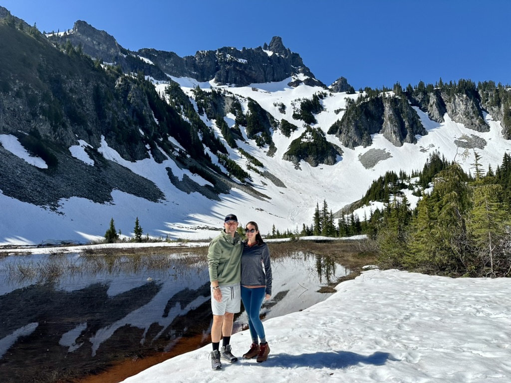 A couple posing in a snowy meadow next to Snow Lake and rugged mountain peaks in the background at Mount Rainier National Park.